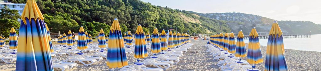 Image depicts the beach front with many yellow and blue umbrellas lined up.