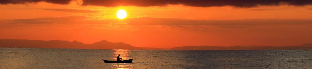 A view of the ocean with a small boat and the sun setting behind it.